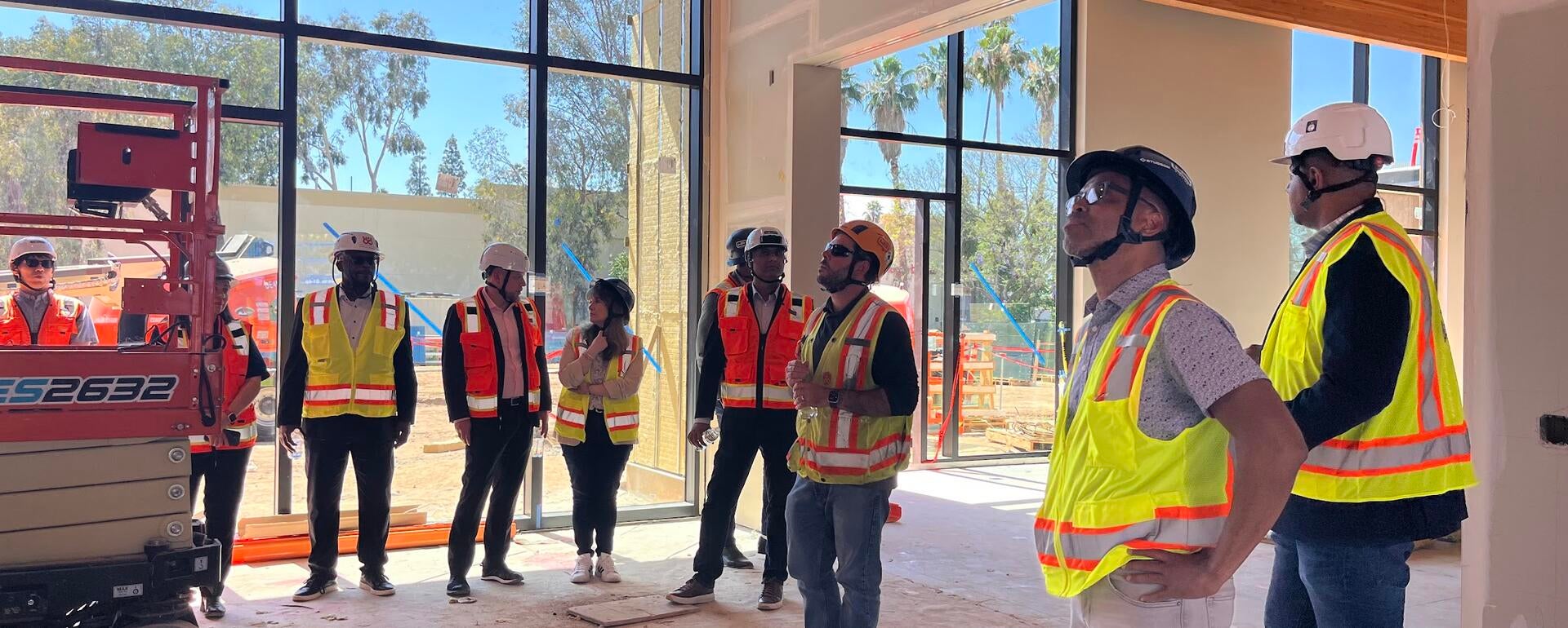 A group Cisco employees and UC Riverside employees wearing hard hats and safety vests inside of the construction site of the SoCal OASIS Park building.